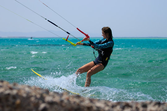 Kite surfing girl in sexy swimsuit with kite in sky on board in blue sea riding waves with water splash. Recreational activity, water sports, action, hobby and fun in summer time. Kiteboarding sport