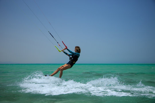 Kite surfing girl in sexy swimsuit with kite in sky on board in blue sea riding waves with water splash. Recreational activity, water sports, action, hobby and fun in summer time. Kiteboarding sport