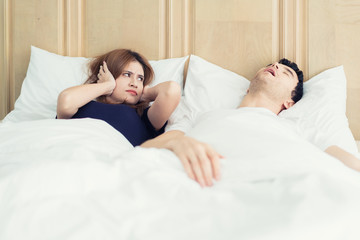 Obraz na płótnie Canvas Annoyed Asian wife blocking her ears from noise of husband snoring in bedroom at home. Young couple have problem with man's snoring.