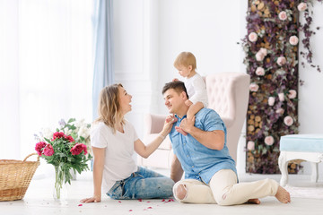Young parents play with their young child in a spacious bright room. Mom and Dad hug and kiss each other