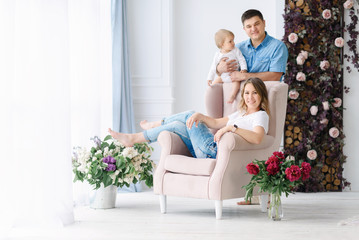 Young parents play with their young child in a spacious bright room. Mom and Dad hug and kiss each other