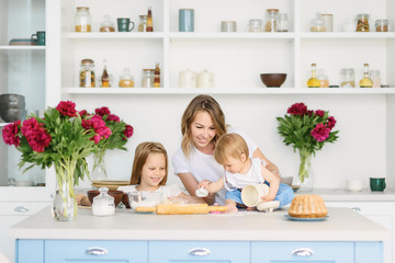 A young mother with her two children is preparing tasty and healthy food in a large and bright kitchen. woman teaches children how to make dough