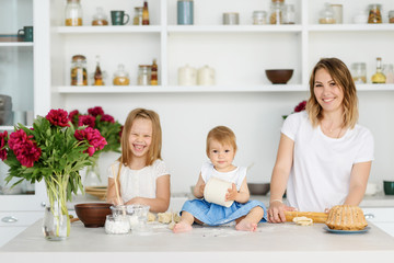 Obraz na płótnie Canvas A young mother with her two children is preparing tasty and healthy food in a large and bright kitchen. woman teaches children how to make dough