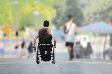 ASL affected young man on a wheel chair in the street among other people. Empty copy space for Editor's text.