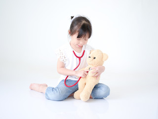 Portrait Asian kid girl playing doctor with her teddy bear over white background.