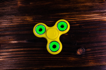 Yellow fidget spinner on wooden desk. Top view