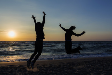 Fototapeta premium Two happy girls having fun and standing with raised arms on background of sunset sea.