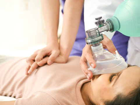 Doctors giving CPR to a woman lying on a bed in the emergency room.