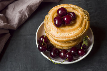 Custard cake rings with cherry on a plate on a dark background. Selective focus. Copy space