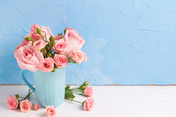 Background with pnk roses flowers in blue cup against  blue textured wall.