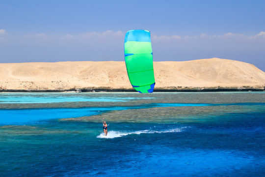 Kite surfing girl in sexy swimsuit with kite in sky on board in blue sea riding waves with water splash. Recreational activity, water sports, action, hobby and fun in summer time. Kiteboarding sport
