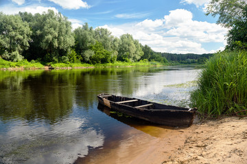 Old rowing boat on green summer beach under blue sky with white clouds at noon Neman River Grodno Belarus