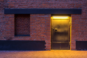 Night view. The entrance to the warehouse. A steel door in a brick wall.