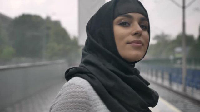 Young muslim woman in hijab is waiting for train on railway station, raining, religion concept, urban concept. weather concept