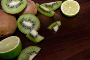 Naklejka na ściany i meble Sliced kiwi with lime on a dark brown wooden table