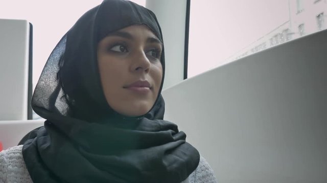 Young muslim woman in hijab is watching in window in bus, rainy weather, transport concept, urban concept