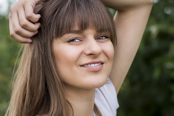 Natural portrait of cute beautiful girl holding her hair in hands and smiling in summer park. Pretty caucasian woman in good mood.