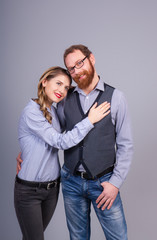 Beautiful young woman and young man are standing in an embrace on a gray background in the studio