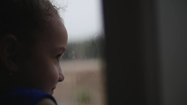 Child looks at the rain behind the window. Stock Footage.