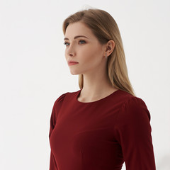 Young blonde woman in cherry red dress standing and posing on white background. Female with long straight hair.