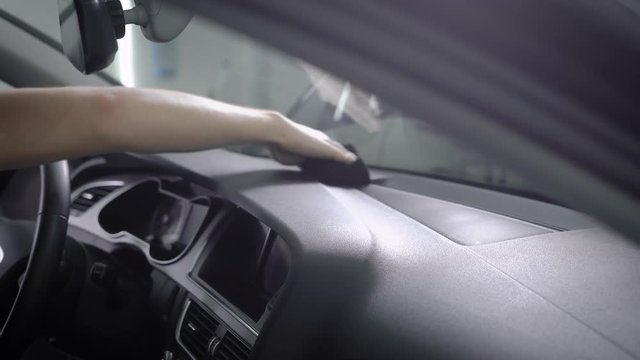 washerman is wiping control panel of modern auto by black sponge, sitting inside, close-up of hand