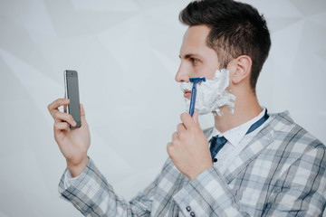 A smiling man of pleasant appearance shaves his face with a machine tool. Advertising of shaving accessories