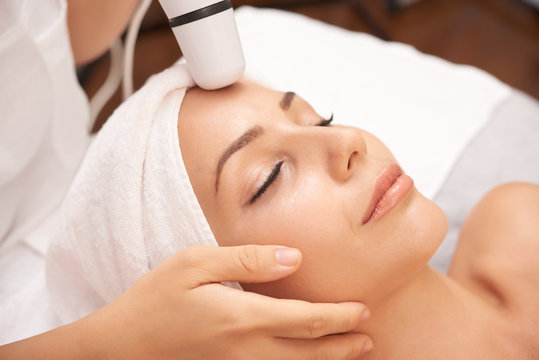 Relaxed woman enjoying facial beauty procedure carried out with special electric device