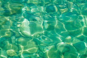 Texture of azure clear sea water with reflection of sun rays on a transparent bottom, background