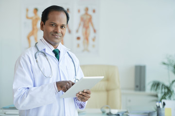 Portrait of Indian doctor using touchpad for work - obrazy, fototapety, plakaty