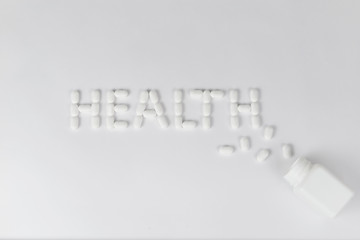 White pills on white background word health pouring out of the white bottle.