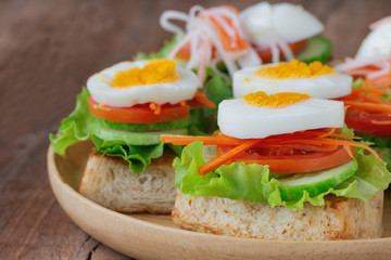 Open faced sandwich with toast lettuce tomato carrot cucumber and boil egg on wooden plate in close up view. Delicious breakfast for family served on wood table. Homemade and healthy food concept.
