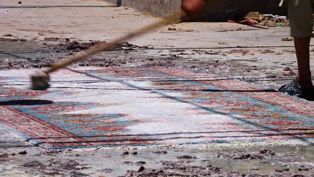 A medium shot of a carpet being cleaned by two people. The carpets are made in Kabul.