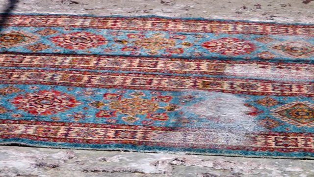 A medium shot of a carpet being cleaned by two people. The carpets are made in Kabul.