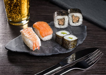 Sushi and a glass of beer on a gray stone.