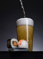 Sushi and a glass of beer on a gray stone.