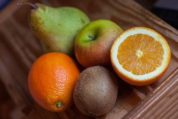 Assortment of fruits on a wooden surface: pear, apple, kiwi and one and a half orange.