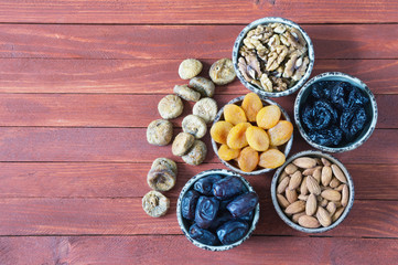 Various nuts and dried fruits (walnuts, almonds, prunes, dried apricots, date fruits, figs ) on  wooden background. Flat lay. Free space for text