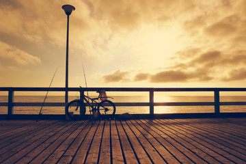 Fototapeta na wymiar Fisherman bicycle with fishing rods on wooden bridge. Toned. Bicycle on sea bridge at sunset. 