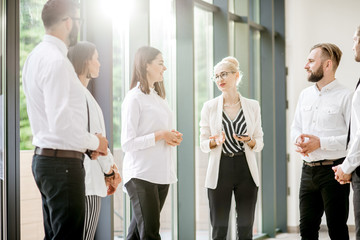 Business people strictly dressed in white having a conversation standing together at the office hall with sunlight indoors