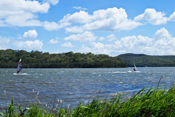 Fototapeta na wymiar Two windsurfers struggling with a strong wind on Narrabeen Lagoon in Sydney.