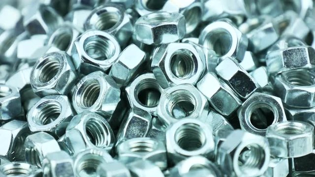 Stack of shiny nuts rotating on a mirror background. Pile of fastener with a threaded hole that forms a connection with a screw, bolt or stud