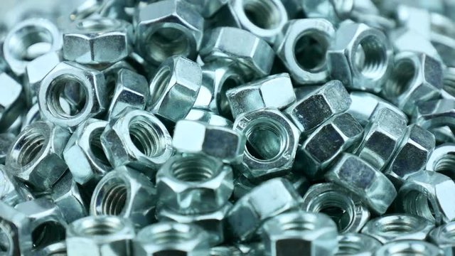 Stack of shiny nuts rotating on a mirror background. Pile of fastener with a threaded hole that forms a connection with a screw, bolt or stud