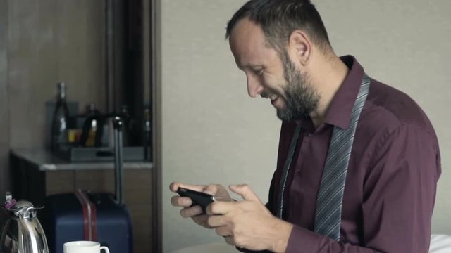 Young, happy businessman playing game on phone during breakfast in hotel
