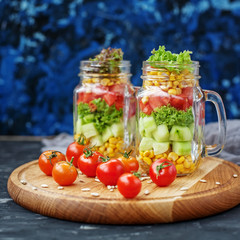 Salad with tomatoes and corn and cucumbers and lettuce. Wooden b