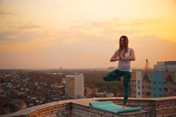 Fototapeta na wymiar Tree Pose(Vrksasana) Young Caucasian woman meditating on the roof.