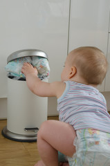 baby touching the garbage can full of  used dirty diapers.  view from back. selective focus   .