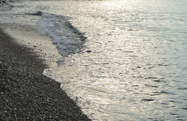 Shiny silver water on the sea pebble beach, early morning sunrise