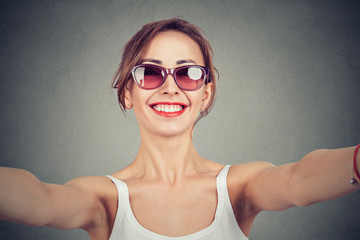 Cheerful woman looking at camera and taking selfie on gray background.