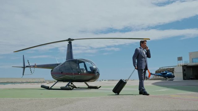 Businessman talking on cellphone near private helicopter