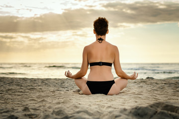 Fototapeta na wymiar beautiful woman in a black swimsuit meditating on the beach at sunset